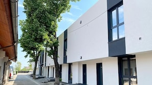 Un hotel moderno con fachada blanca y limpia y detalles oscuros. Se observan múltiples ventanas y puertas, y un árbol en primer plano.