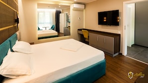 Una habitación de hotel con cama, escritorio, silla, televisor y espejo.
