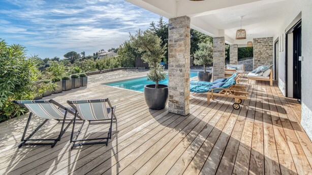 Terraza de madera con sillones de descanso, piscina y pilares de piedra.