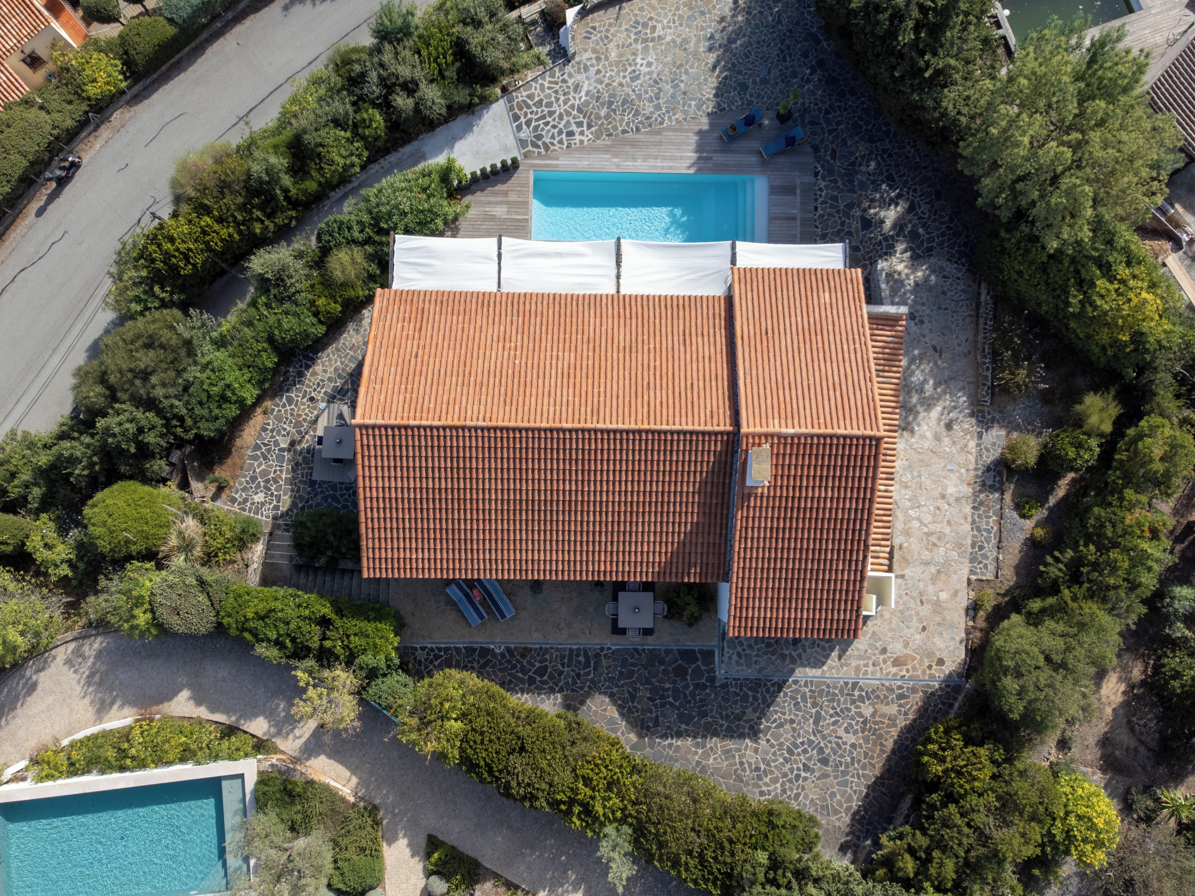 An aerial view of a property with a swimming pool, a patio area with sun loungers, and a stone pathway.