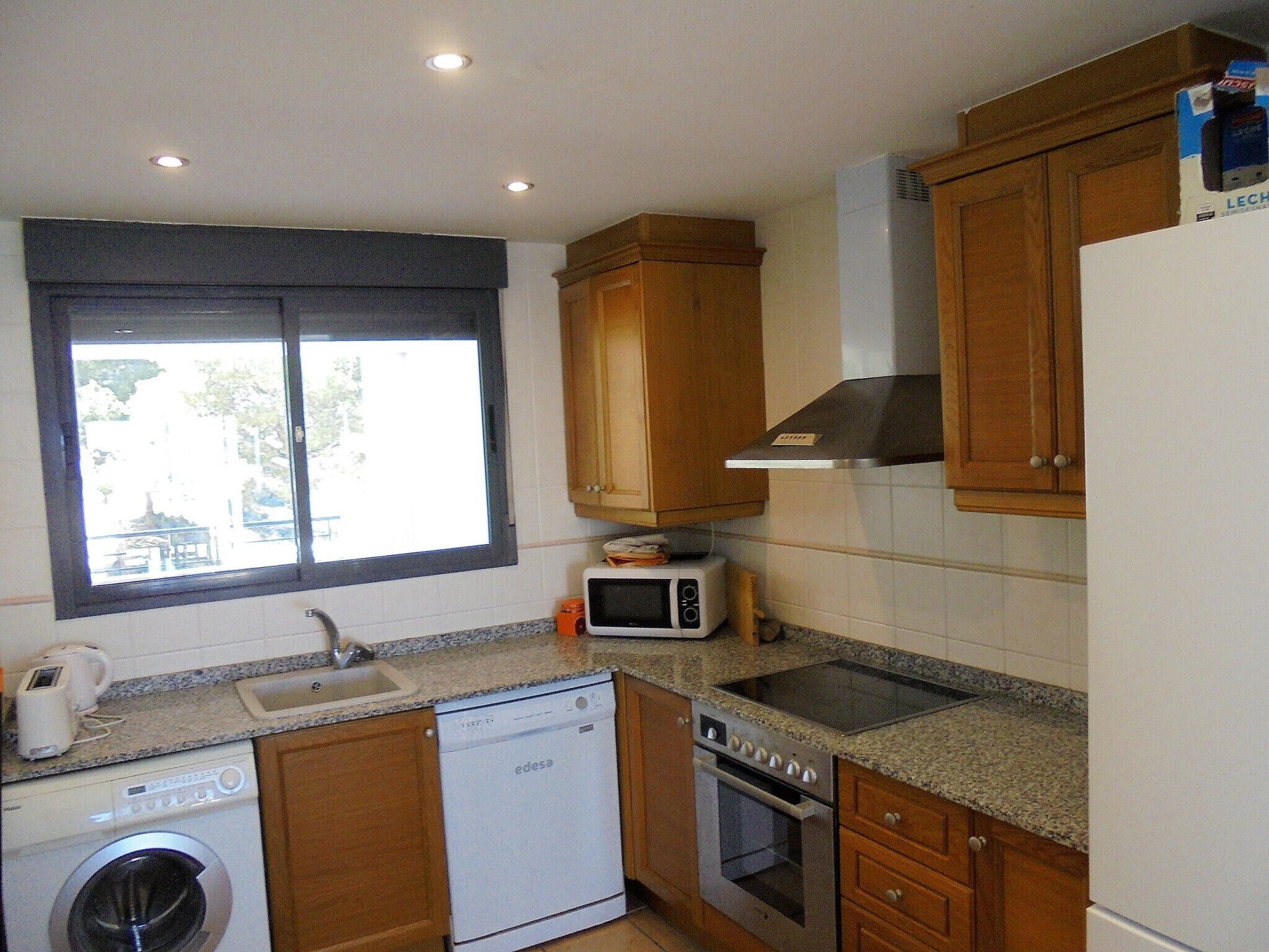 Una cocina compacta con armarios de madera, lavavajillas, microondas, horno y ventana con vistas.