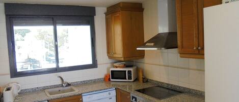 Una cocina compacta con armarios de madera, lavavajillas, microondas, horno y ventana con vistas.
