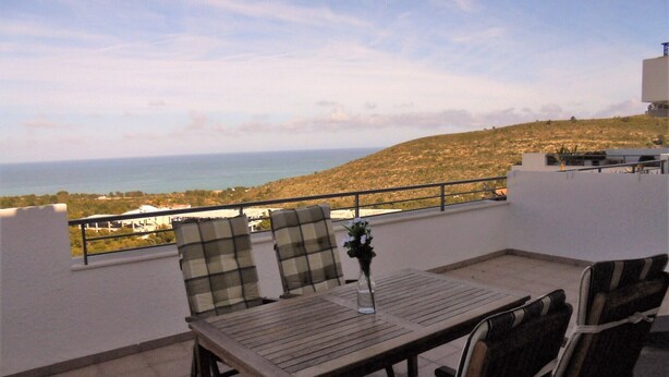 Une terrasse avec une table et des chaises, offrant une vue sur un paysage côtier.