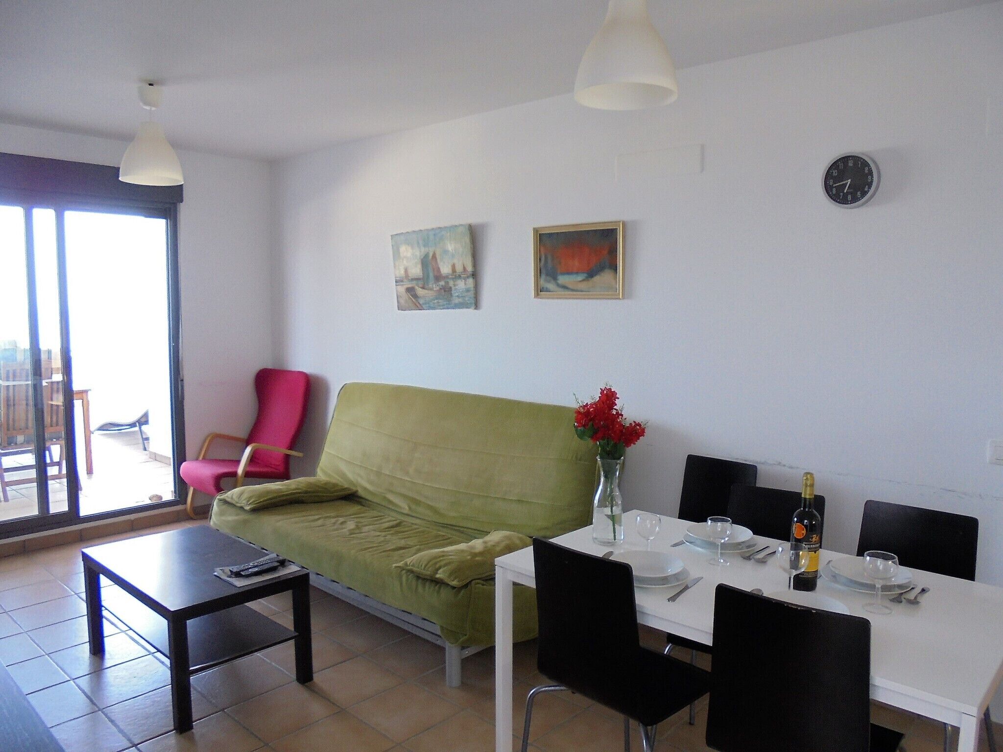 A living room with a green sofa, a dining table set for two, and a balcony with a chair.