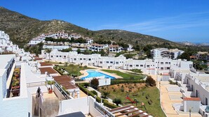 Un quartier résidentiel en bord de mer, avec des bâtiments blancs, une piscine et un paysage vallonné en arrière-plan.