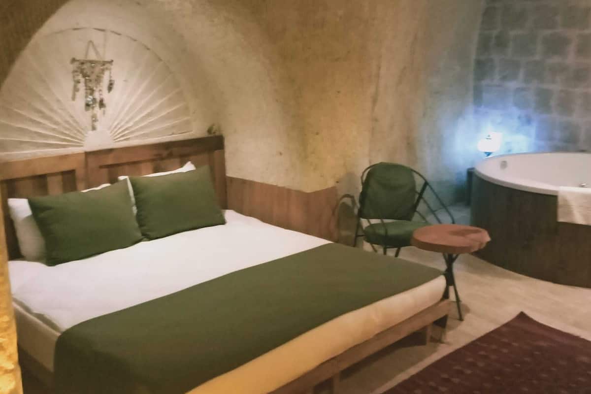 A bedroom with a bed, a chair, a small table, and a stone wall.