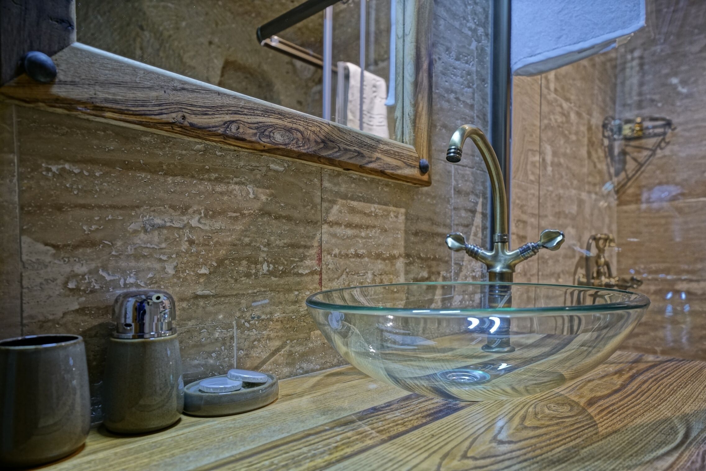 A wooden countertop with a glass bowl sink, a faucet, and a small metal container.