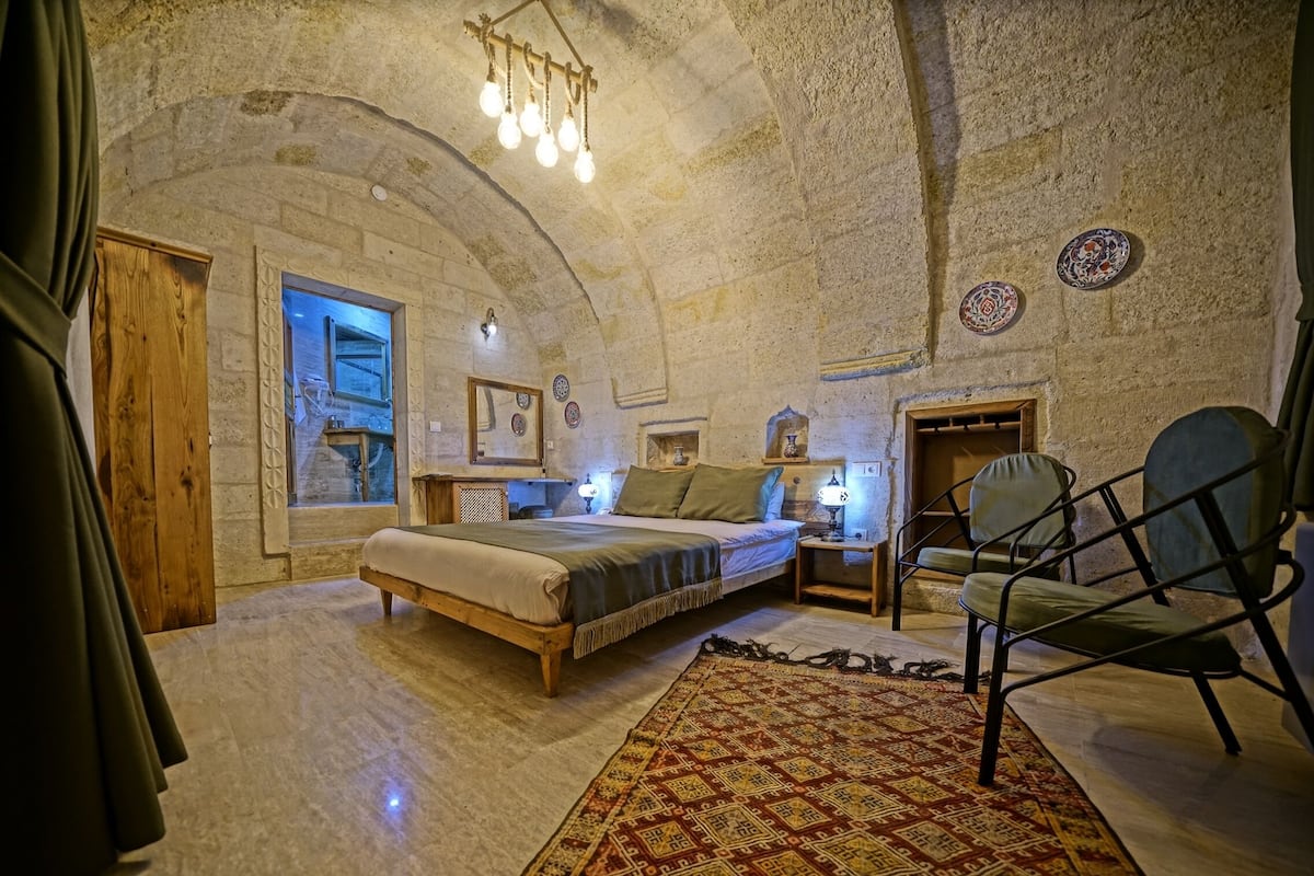 A rustic stone-walled bedroom with a bed, a chair, and a nightstand.