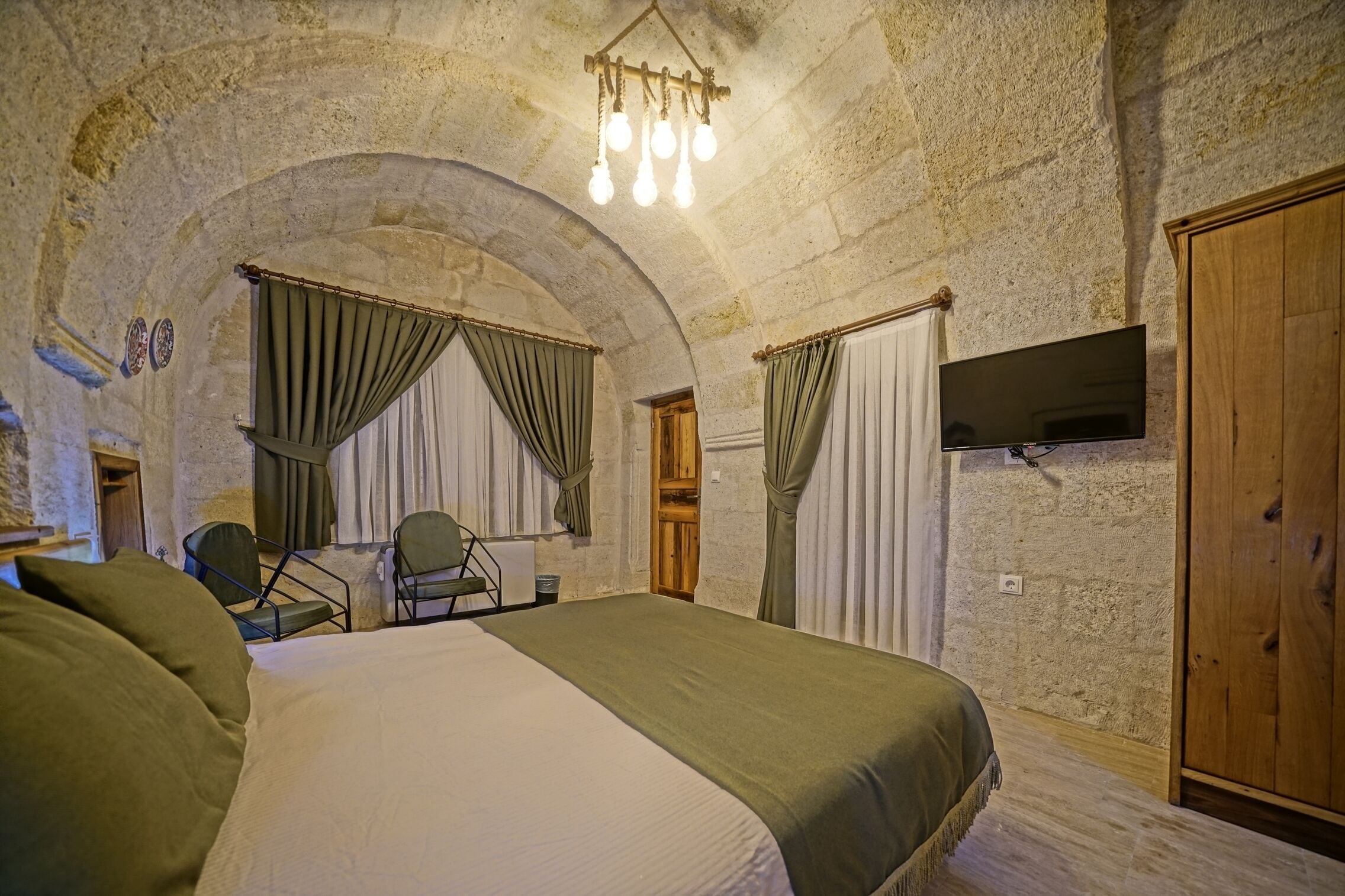 Una habitación con una cama grande, un televisor montado en la pared y un arco de piedra.