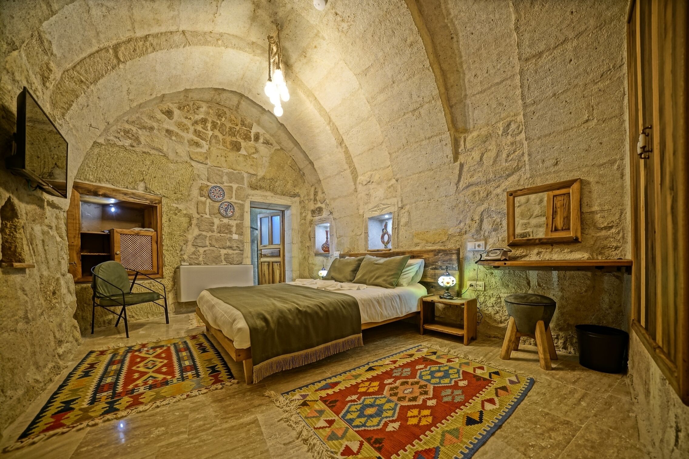 A cozy, stone-walled bedroom with a bed, a chair, a nightstand, and a small stool.