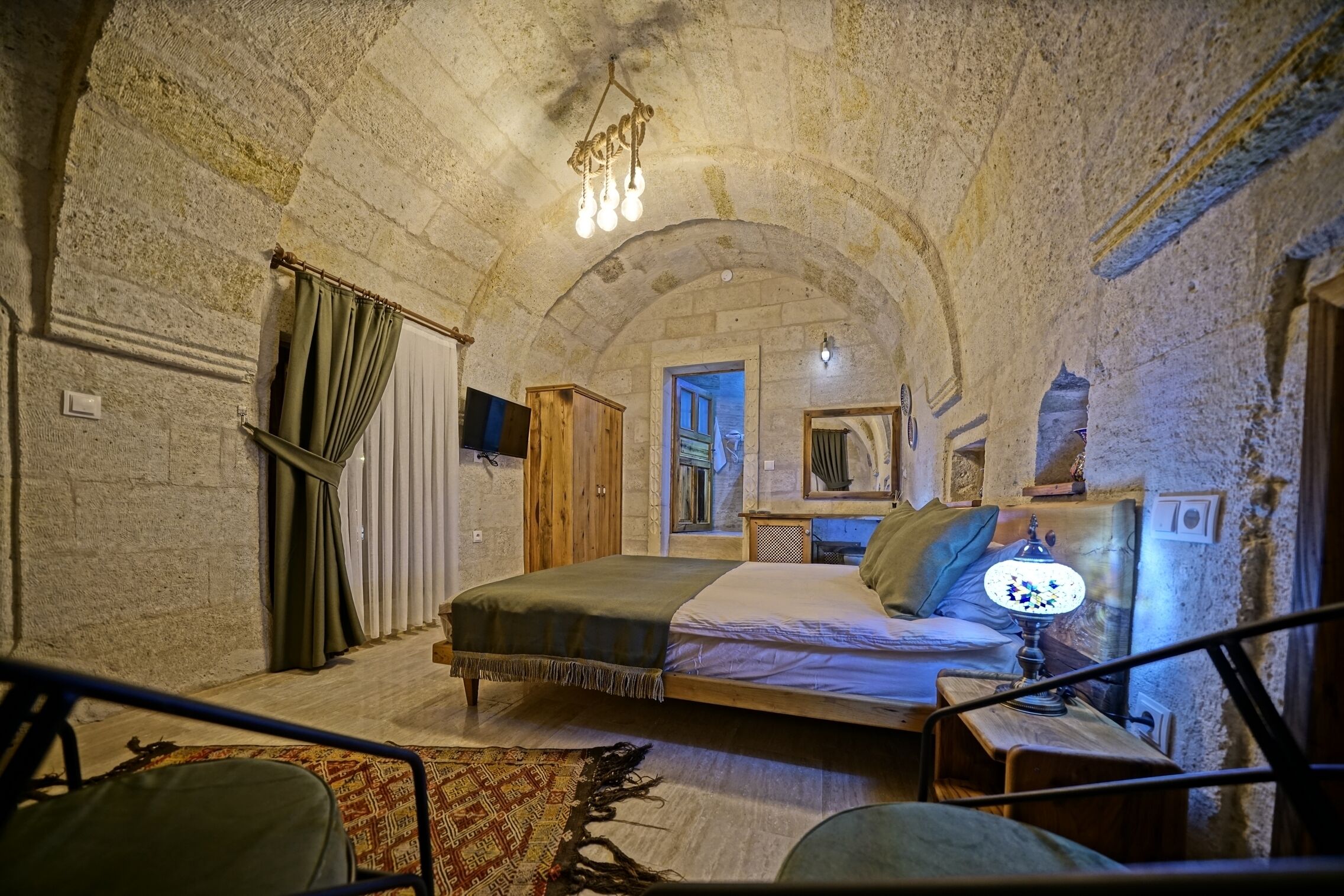 Une chambre rustique avec un plafond en pierre, un lit doté d’une tête de lit en bois, une table de chevet avec une lampe et une vue sur un mur en pierre.