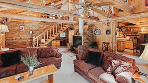 A rustic cabin interior with wooden floors, a fireplace, a dining area, and a staircase leading to an upper level. -  Beautiful Log home outside of Sisters, OR (Sisters)