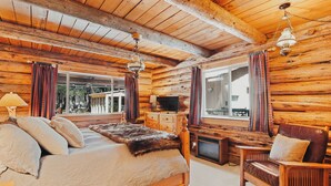 A log cabin bedroom with a bed, a wooden chair, a television, and a fireplace. -  Beautiful Log home outside of Sisters, OR (Sisters)