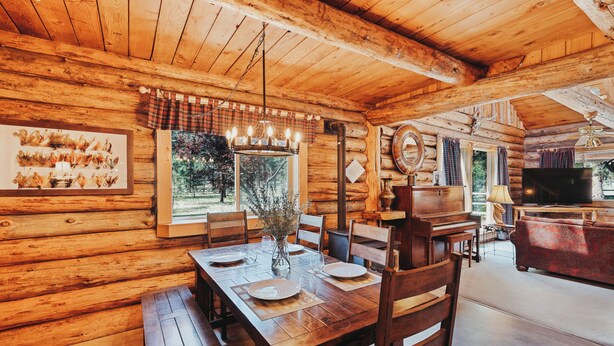 A wooden cabin interior with a dining area, a piano, and a television. -  Beautiful Log home outside of Sisters, OR (Sisters)