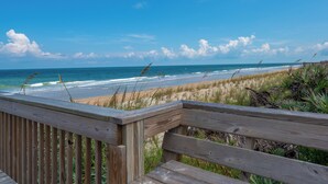 A wooden deck overlooking a beach with waves and a clear sky.