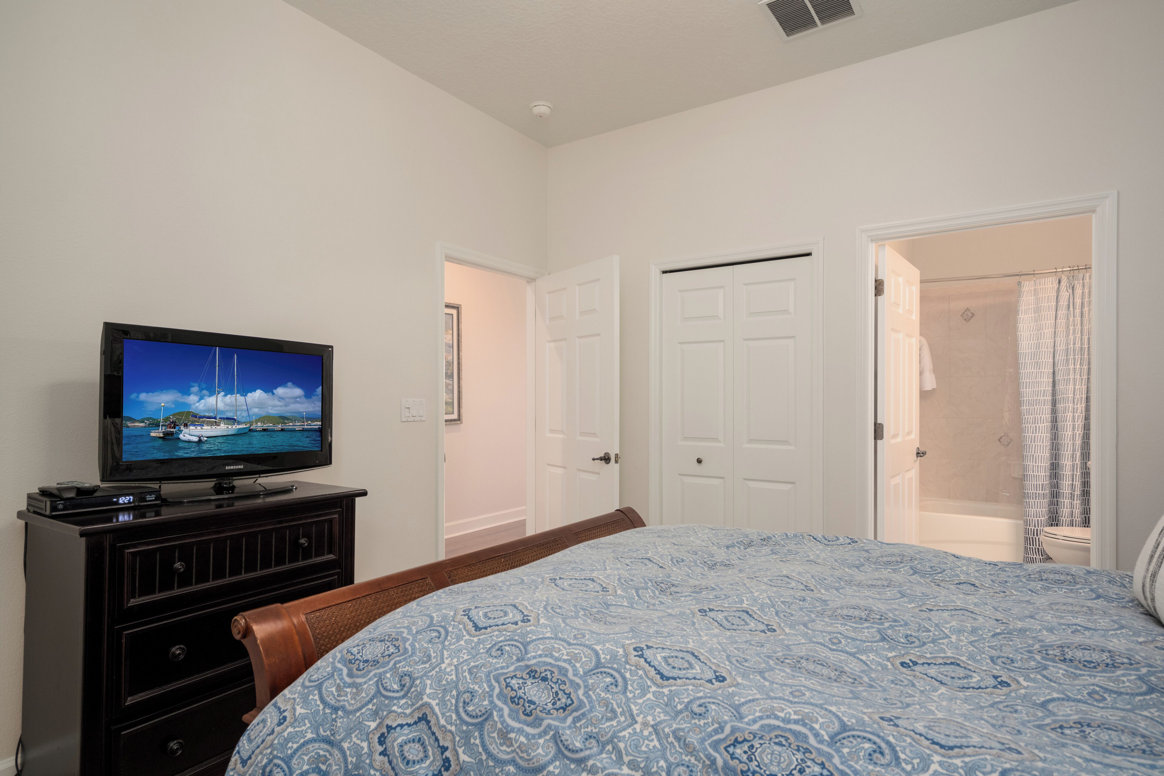 A bedroom with a bed, a TV on a dresser, and a bathroom with a shower curtain.