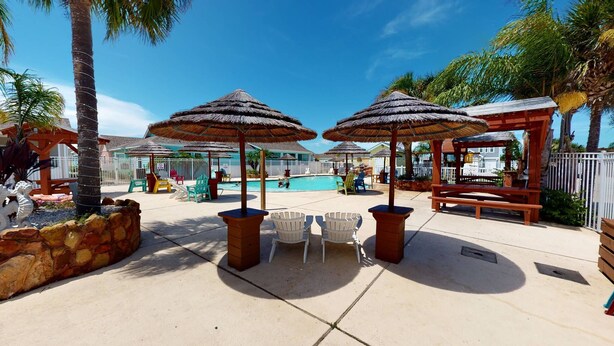 A poolside area with thatched umbrellas, lounge chairs, and a wooden bench. - PB302 Community Pool and Parking for 3 (Port Aransas)