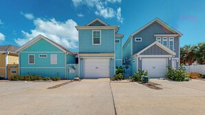 A row of three houses with attached garages, a clear blue sky, and a well-maintained driveway. - PB302 Community Pool and Parking for 3 (Port Aransas)