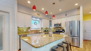 A modern kitchen with white cabinets, a granite countertop, stainless steel appliances, and pendant lighting. - PB302 Community Pool and Parking for 3 (Port Aransas)