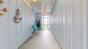A hallway with light blue walls, a ceiling fan, a chair, and a plant. - PB302 Community Pool and Parking for 3 (Port Aransas)