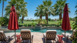 A poolside area with lounge chairs and red umbrellas, surrounded by palm trees and a view of a golf course. - FALL GETAWAYS 25% OFF - Private and Serene - Room for the whole Family (La Quinta)