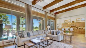 A spacious living room with a sectional sofa, a glass coffee table, and a large window with a view of palm trees. - FALL GETAWAYS 25% OFF - Private and Serene - Room for the whole Family (La Quinta)