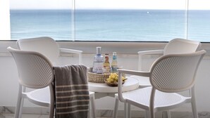 Ein Balkon mit zwei weißen Stühlen, einem kleinen Tisch mit Flaschen und einer Obstschale, mit Blick auf das Meer.