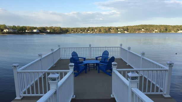 A deck with a table and chairs, overlooking a calm lake with a distant shoreline. - Direct waterfront vacation rental, family friendly, pets allowed (East Lyme)