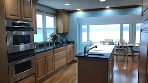 A modern kitchen with wooden cabinets, stainless steel appliances, and a large window providing a view of the outdoors. - Direct waterfront vacation rental, family friendly, pets allowed (East Lyme)