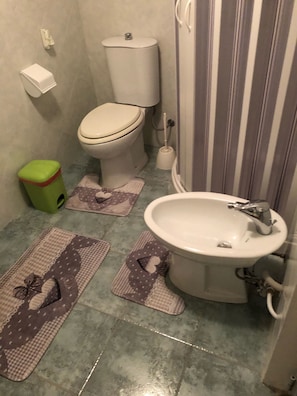 A bathroom with a toilet, sink, and a green trash bin.