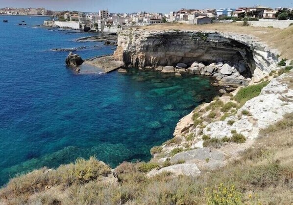 A coastal landscape with clear blue waters, rocky cliffs, and a distant town.