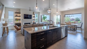 A modern kitchen with a large island, dark cabinetry, and pendant lighting.