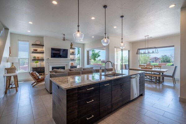 Cocina moderna con una isla grande, armarios oscuros e iluminación colgante.