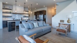 A modern kitchen with a grey sofa, a wooden chair, and a dining area.