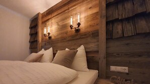 Un lit avec une literie blanche et plusieurs oreillers, une tête de lit en bois avec des lampes fixées au mur, et une prise électrique visible.