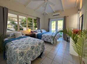 Ein Hotelzimmer mit zwei Betten, einem Deckenventilator, einem Fenster mit Vorhängen und einer Zimmerpflanze.