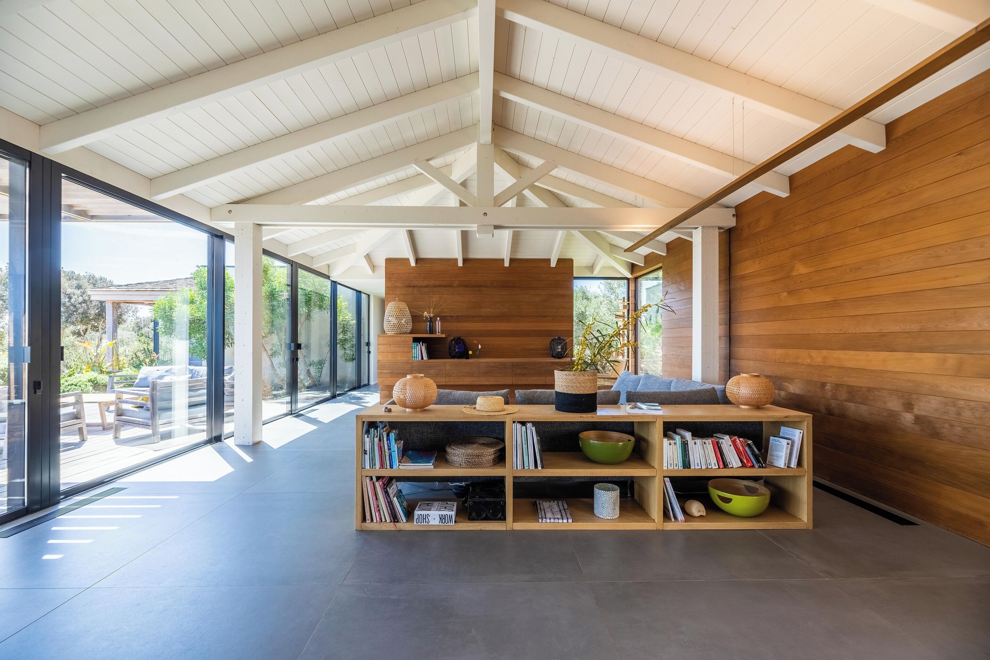 Un intérieur moderne avec une bibliothèque en bois, un canapé et une grande fenêtre donnant sur l’extérieur.