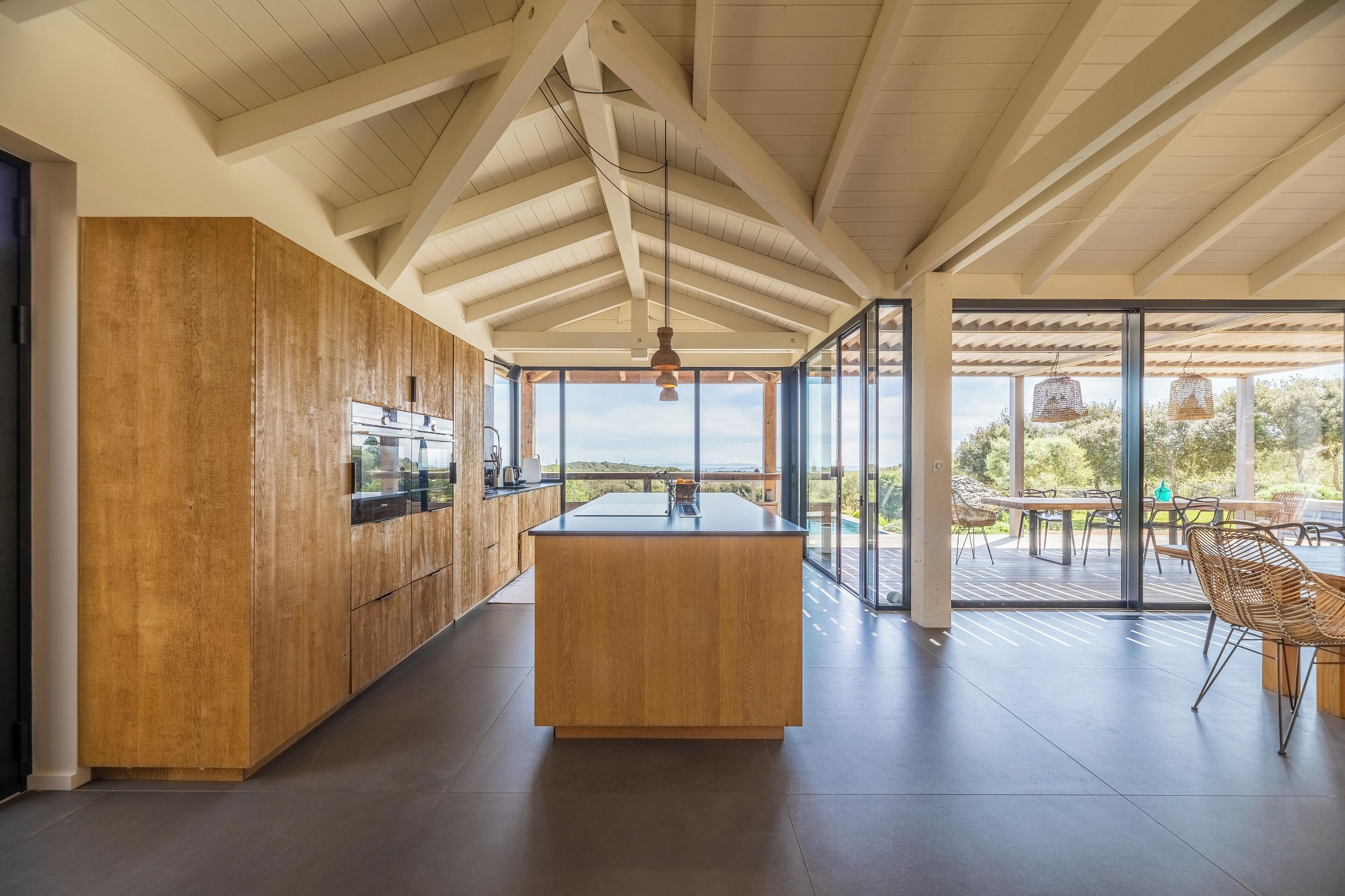 Une cuisine moderne dotée d’un îlot central, de meubles en bois et de grandes fenêtres offrant une vue sur l’extérieur.