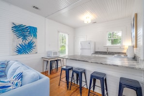 Una cocina moderna con paredes de madera blanca, una isla central con taburetes altos, un microondas y un refrigerador.