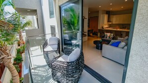 A modern apartment with a glass door leading to a balcony, furnished with wicker chairs and a sofa, and a kitchen visible through the door. - Waykiri Unit C-08 Luxurious New Apartment, Noord (Noord)