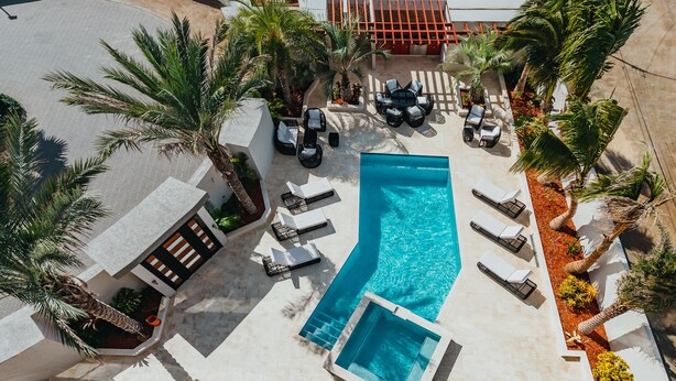 An aerial view of a pool area with lounge chairs, palm trees, and a swimming pool. - Waykiri Unit C-08 Luxurious New Apartment, Noord (Noord)