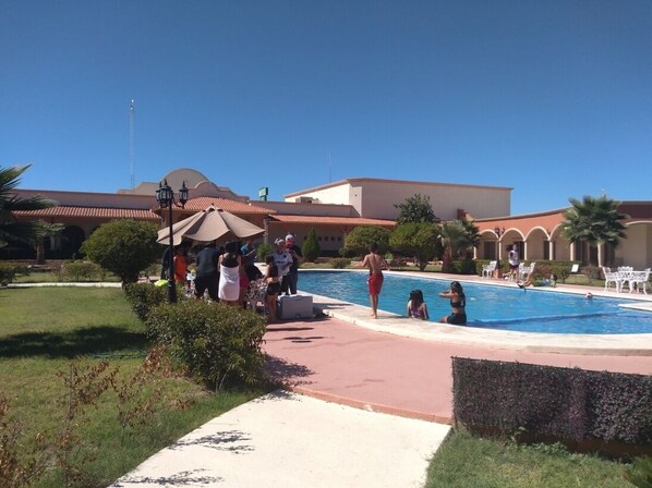 Un área de piscina con un pabellón, palmeras y un edificio con techo de tejas rojas.