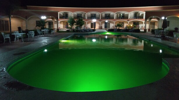 A pool area with a green-lit pool, outdoor seating, and a building with multiple balconies. - Hotel Jimenez Plaza (Jimenez)