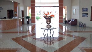 A spacious lobby with a reception desk, a large decorative vase with flowers, a leather sofa, and a clock on the wall. - Hotel Jimenez Plaza (Jimenez)