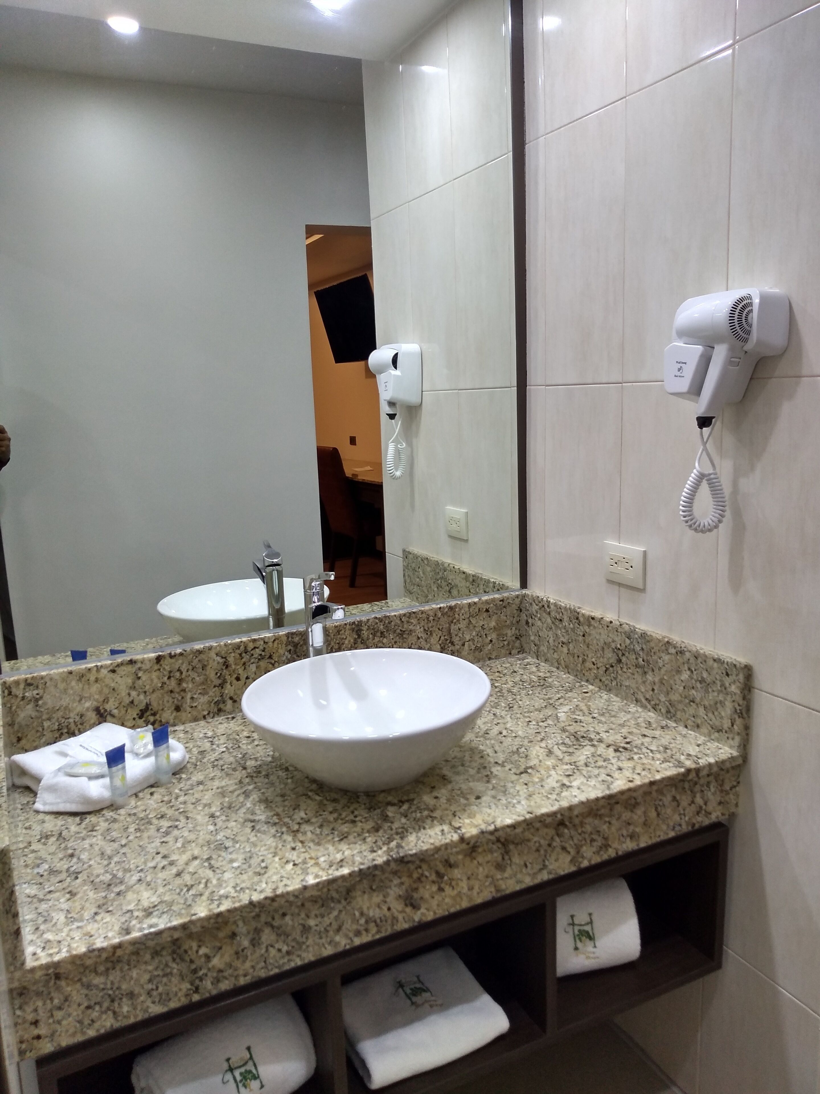 A bathroom with a granite countertop, a white sink, a hairdryer, and a mirror.