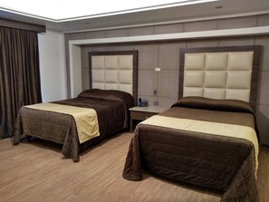 Habitación de hotel con dos camas, cada una con cabecero y mesita de noche.