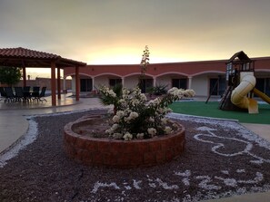 Un patio con un macizo de flores en el centro, mobiliario exterior y un parque infantil.