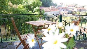 Un balcón con una mesa y sillas de madera, un jarrón con flores y vistas a casas al fondo.