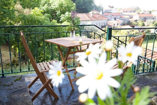 A balcony with a wooden table and chairs, a vase with flowers, and a view of houses in the background. - Casa da Eira - into the nature (Macieira de Alcôba)