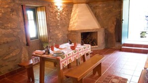 Una habitación rústica con pared de piedra, chimenea, una mesa de comedor con mantel y un banco.